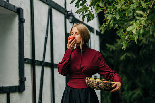 Woman in vintage dress smells an apple outside an old house
