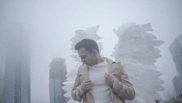 Depressed fallen angel standing in misty metropolis environment with negative space