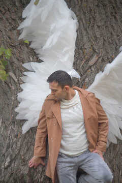  Sad man with white angel wings leaning on textured tree trunk with copy space