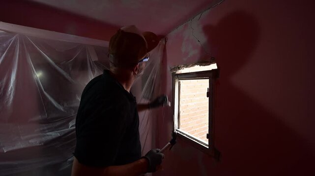 Man demolishing a wall with hammer and chisel during home renovation