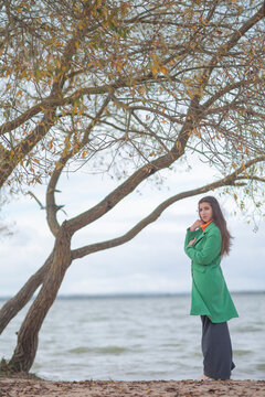 Beautiful young woman in green coat posing on autumn lakeside with copy space