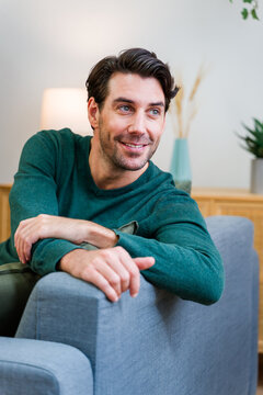 White man smiling seated on gray sofa in living room