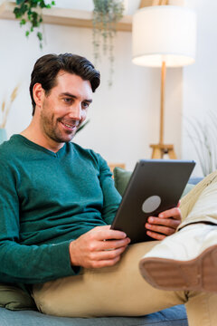 White man sitting on couch using tablet in living room indoors