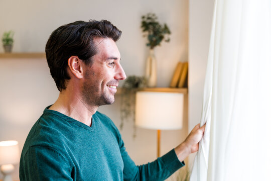 White man smiling and pulling back curtain