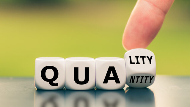 Human finger flipping a white dice block to change the word quantity to quality