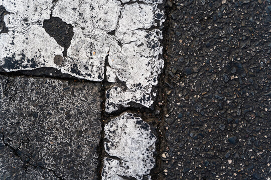 Closeup of worn and cracked white road markings on asphalt surface