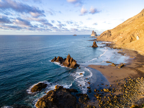 A single sea stack breaks the water where black sand meets the Anaga cliffs on Tenerife. A clean establishing view of the island's wildest stretch of coast.