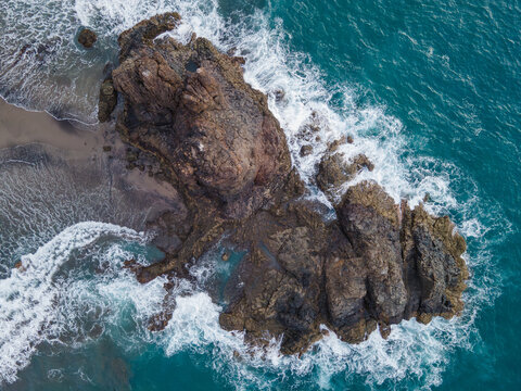 A closer overhead pass tightens the frame on the Roque de Benijo rock formation as waves break around it. A near twin of the wider top down view on Tenerife.