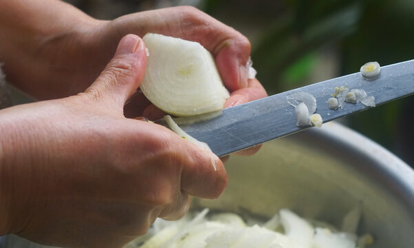 Close-up of hands slicing a white onion with a knife.