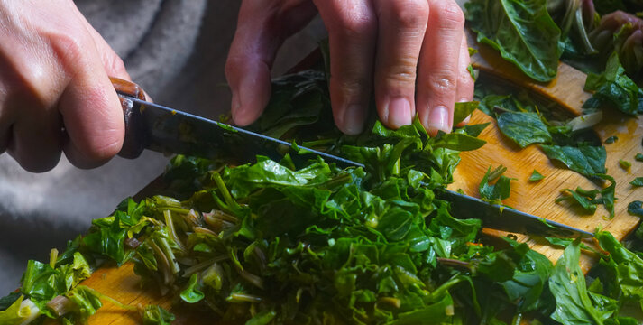 Top view of hands chopping fresh green spinach for traditional Uzbek somsa.