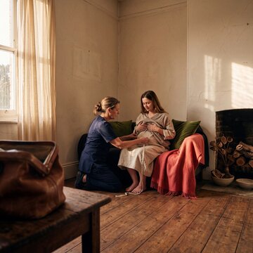 Midwife measuring the belly of a pregnant woman with a tape measure during a home prenatal checkup visit