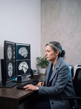 Professional Female Neurologist Analyzing Brain MRI Scans on Dual Monitors in Medical Office