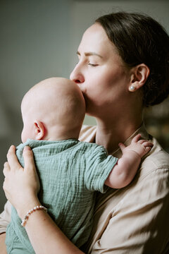 Vertical shot of Caucasian mother holding and kissing baby child at home, expressing maternity bonding and love. Image suitable for parenting campaigns and family lifestyle marketing