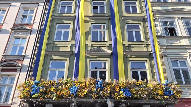 ​Historic building facade decorated with blue and yellow Ukrainian national flags and vibrant sunflower floral arrangements on a balcony in Rynok Square, Lviv, Ukraine.