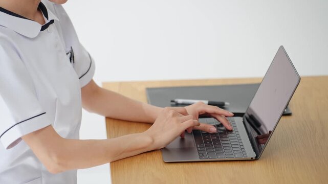 A woman in a white coat using a laptop. Nurse, caregiver, medical office worker, hospital, clinic, DX, data entry, electronic medical record, doctor.