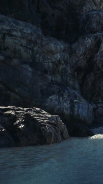 Rocks rise steeply from the waters edge, showing rough textures and dark colors. The scene is located along a coastline where water meets land.