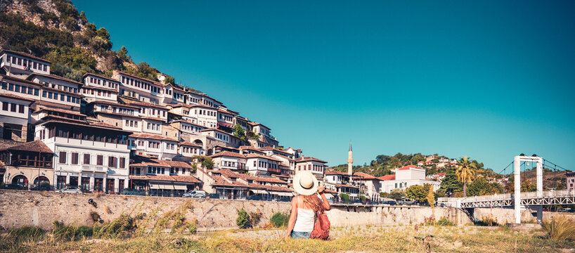 female tourist with hat sitting looking at Ottoman houses in historic old town of berat albania