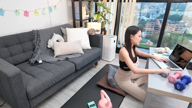Asian Woman Working on Laptop and Exercising with Dumbbell at Home