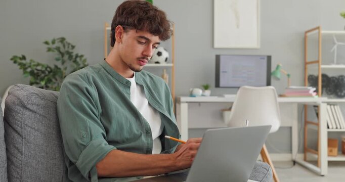 Young man student uses laptop for online learning. On a sofa at home, he works with a computer for flexible remote education and digital coursework. Ideal for modern self paced study.