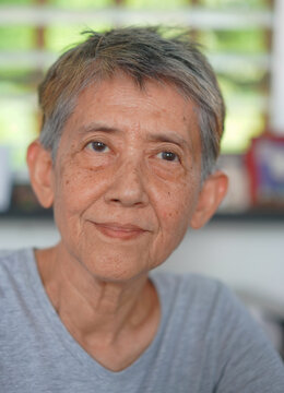 Elderly Gay Woman Portrait: Close-up portrait captures the wise gaze and gentle smile of an Asian senior lesbian woman, her short, gray hair framing a face etched with the stories of a lifetime.