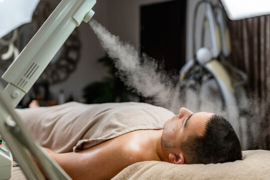 Acne treatment for a young man receiving facial steam therapy in beauty salon, preparing the skin for deep cleansing, pore care and professional skincare.