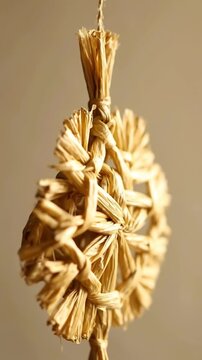 Hanging woven dried fiber ornament slowly rotating to reveal intricate natural texture and braided construction against a warm neutral background in close-up decorative home setting