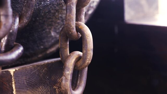 Heavy rusty iron chain hanging and swaying in motion next to a rustic wooden beam. Detailed oxidized steel texture