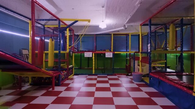 A fake drone shot moves through an empty indoor children's entertainment center featuring a red and white checkered floor and various colorful climbing structures.