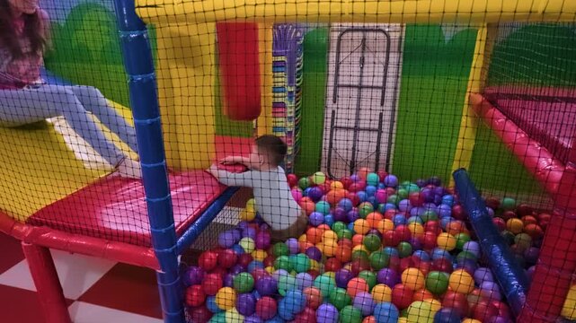 A young Mexican mother and her 2-year-old son have fun racing through a colorful indoor ninja obstacle course with a ball pit in Mexico City, laughing and enjoying their time together.