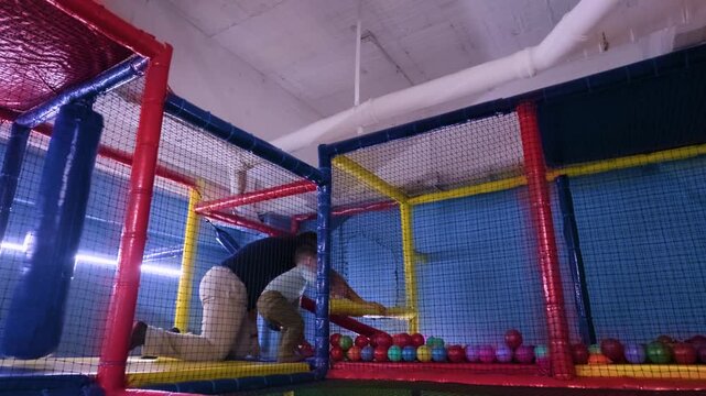 A Latino father and his two-year-old son enjoy an active day at an indoor playground, navigating through a vibrant ninja obstacle course and ball pit in Mexico City.