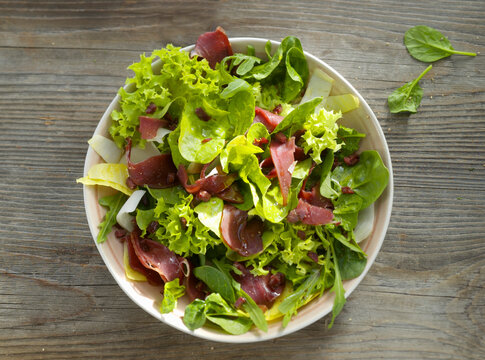 Mesclun salad with raw ham on white plate