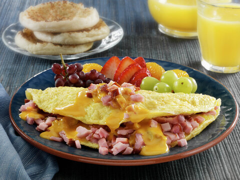 Ham and cheese omelette with fruit, English muffins, and orange juice