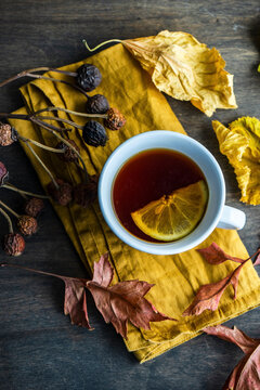 Cup of tea with lemon slice and dry autumn leaves on wooden table