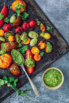 Baked heirloom tomatoes topped with salsa verde on a baking tray