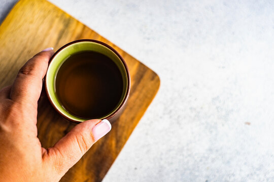 Asian style ceramic tea cup filled with green tea held over wooden