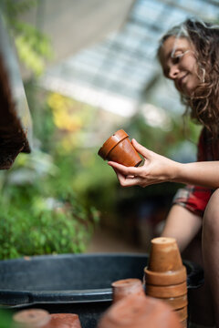 Smiling woman working in botanical garden, sitting cleaning ceramic flower pots in water bucket, cheerful female greenhouse employee washing plant pots in basin, responsibilities and daily tasks.