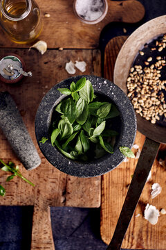 Basil in stone mortar with ingredients for pesto sauce preparation