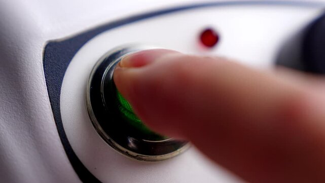 Person finger pushing a circular green start button on a modern electronic medical appliance with small red indicator light
