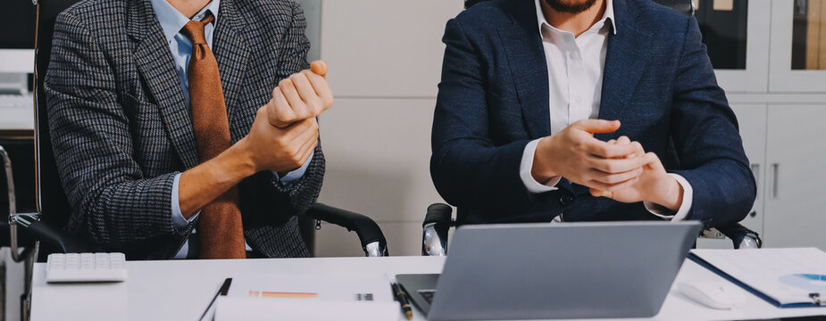 Overworked tired sick man suffer headache ignoring obsessive annoying colleague disturb talk smile discuss project with laptop two multiethnic businessmen diverse men solve teamwork problem in office
