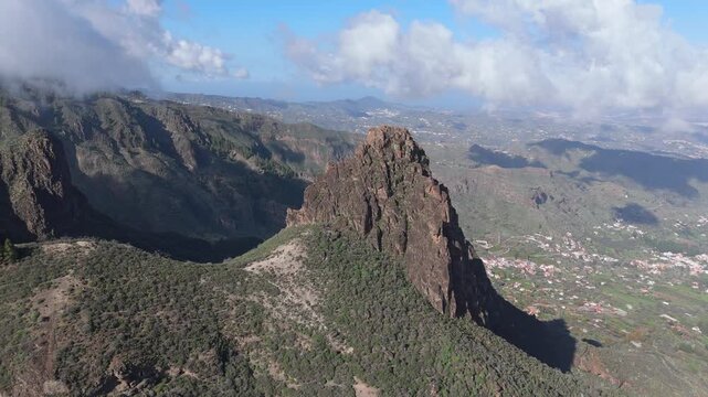 Aerial tracking shot panning right over Roque Grande mountain on Gran Canaria, revealing the rugged volcanic landscape and the charming hamlet of El Rinc&oacute;n in the valley.