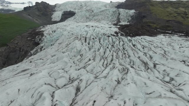 A captivating aerial drone video shows a push in and boom up movement over Fallj&ouml;kull glacier on Iceland. Hikers traverse the rugged ice formations, revealing the vast, remote landscape.