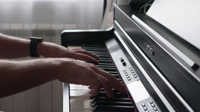 Close view shows a musician's hands moving across electronic piano keys beside sheet music and control buttons in a bright indoor room
