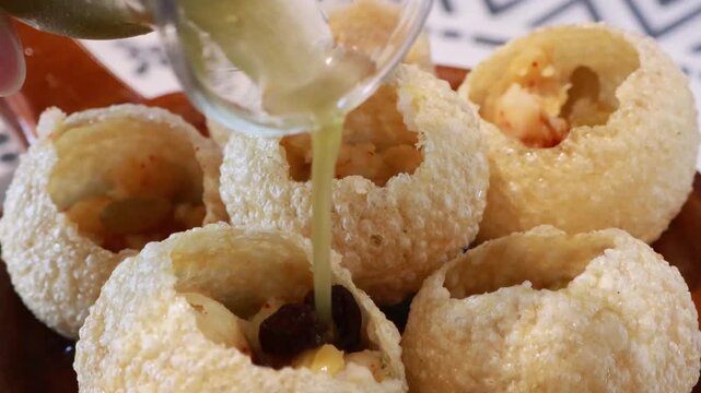 Pouring mint flavored water into traditional Indian panipuri golgappa snack.