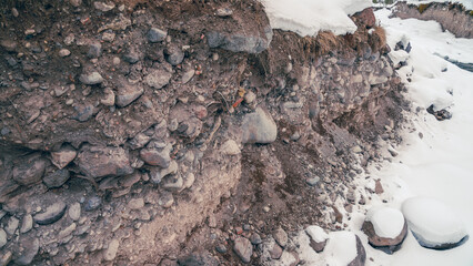 Eroded riverbank with exposed layered soil, gravel, and snow-covered stones in diffuse winter light © ossyffer
