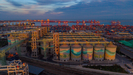 Aerial View of Port‑Side Grain Silos at Dusk, Container Seaport in Background © Zhaorui