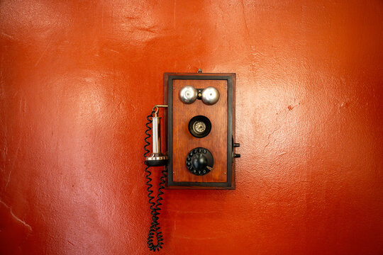 Vintage Wooden Wall Telephone with Rotary Dial on Red Textured Wall.