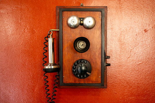 Vintage Wooden Wall Telephone with Rotary Dial on Red Textured Wall.