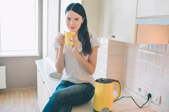 Nice woman sits on curbstone. She poses and ooks on camera. Model holds yellow cup in hands. Also there is a kettle besides her. She is chilling and relaxing.