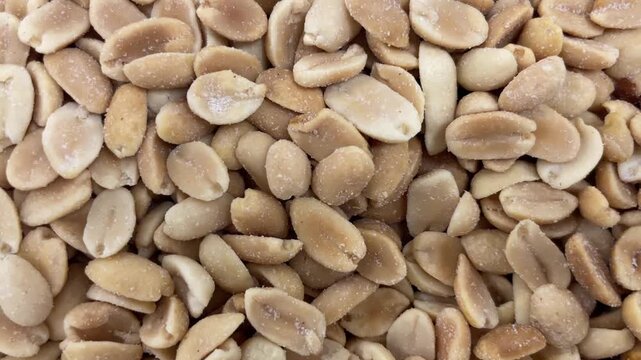 Top-down close-up shelled roasted peanuts with coarse salt crystals. Soft light shows matte surfaces, tan and brown tones, and repeating texture.