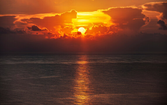 Sun rising through clouds over calm ocean